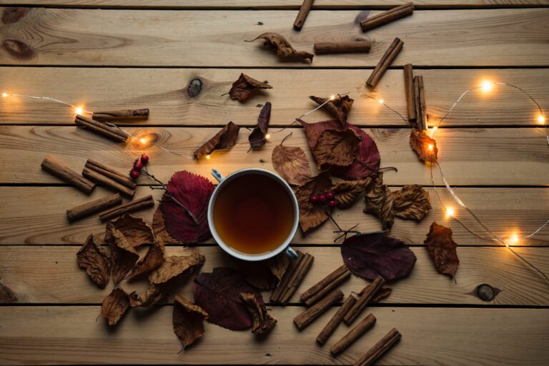 A cup of brown tea surrounded by cinnamon sticks and a few lights.