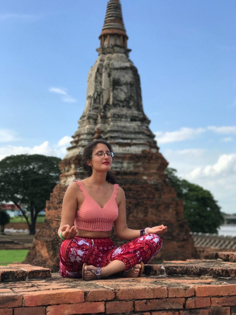 woman in a pink top sits gracefully in front of a traditional pagoda, surrounded by serene natural environment in Thailand