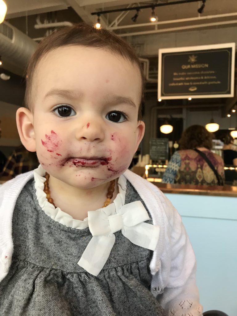 A toddler with a messy face sits happily in a chair, reflecting the fun and messiness of teething experiences.