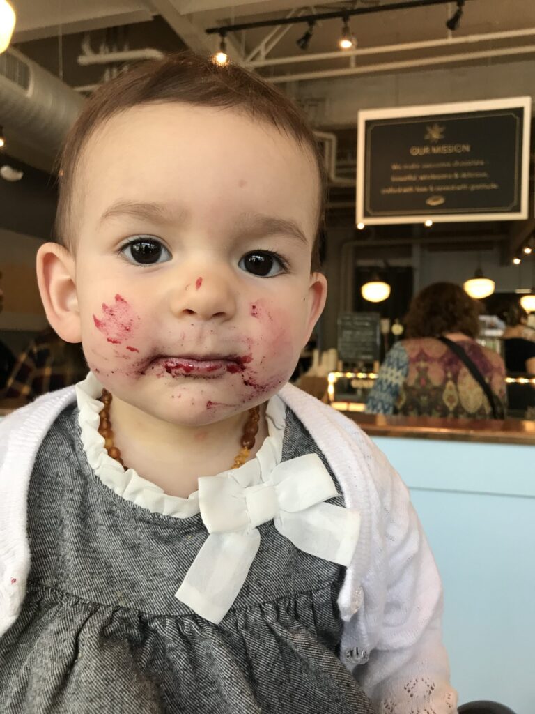 A toddler with a messy face sits happily in a chair, reflecting the fun and messiness of teething experiences.